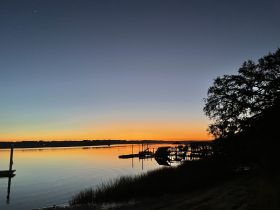 A serene sunset view over calm waters, with silhouettes of docks and trees creating a tranquil atmosphere.