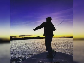 A silhouette of an angler casting a line into the water at sunset, capturing the serene beauty of fishing on the water.