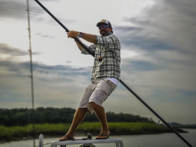 A man stands on the bow of a boat, skillfully fishing with a pole against a scenic backdrop — a perfect capture of an adventurous day on the water.