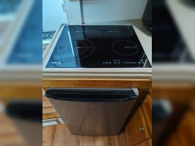 A close-up view of the kitchen area inside a boat, featuring a modern induction cooktop and a compact refrigerator, ideal for onboard meal preparation.