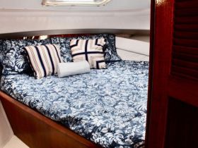 Cozy cabin interior featuring a beautifully made bed with decorative pillows, perfect for relaxing on a sailing adventure.