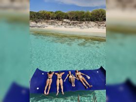 A group of friends relaxes on a floating mat in crystal-clear waters, enjoying a sunny day at the beach — perfect for summer getaways and fun in the sun.