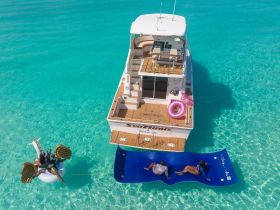 A fun day on the water with friends enjoying a floating mat and inflatable while anchored near a stunning boat in crystal-clear waters.