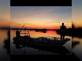 A silhouette of a fisherman casting his line at sunset, with vibrant reflections on the water — a serene moment perfect for fishing enthusiasts.