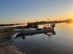A serene sunset view of a fishing boat docked along the shore, reflecting beautifully on calm waters — perfect for tranquil fishing trips or scenic outings.