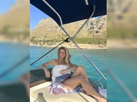 A woman relaxes on the deck of a boat, enjoying the sunny day and stunning coastal views — perfect for a day of leisure on the water.