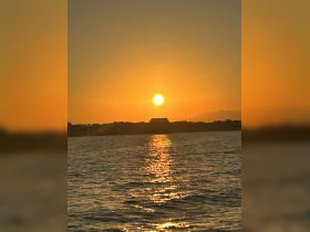 A stunning sunset casts a golden glow over the water, creating a picturesque backdrop perfect for evening boat cruises along the coastline.