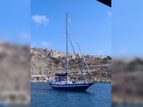 A beautiful sailboat anchored near a rocky coastline, showcasing its elegant design against a clear blue sky — perfect for sailing enthusiasts and coastal adventures.