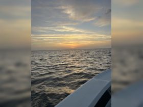 A serene sunset view over the water, captured from the side of a boat, showcasing the tranquil beauty of evening on the sea.