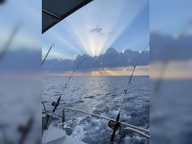 A stunning view of rays of sunlight breaking through clouds over the ocean, with fishing rods in the foreground — a perfect moment for fishing enthusiasts enjoying a day on the water.