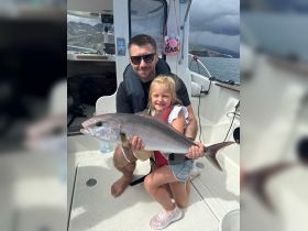 A proud moment as a child holds up a freshly caught fish with an adult on a boat, showcasing the joy of family fishing adventures.