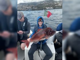 A young boy proudly displays his catch while fishing on a boat, showcasing the excitement of a successful fishing trip in the ocean.