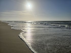 A serene beach scene with gentle waves and a bright sun, capturing the tranquil beauty of the shoreline.