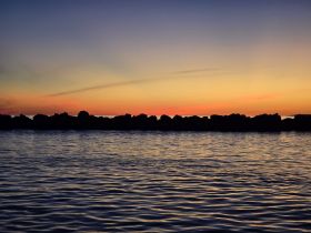 A serene sunset view over calm waters, with silhouettes of rocks in the foreground, creating a tranquil atmosphere perfect for evening reflections.