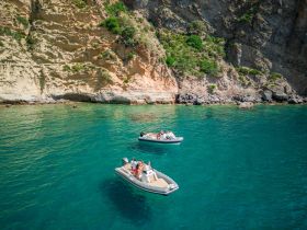 Two boats navigate the crystal-clear waters near a stunning coastline, showcasing a perfect day of adventure and exploration on the water.