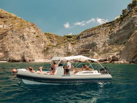 A lively group enjoys a day on the water aboard a boat, soaking up the sun against a stunning coastal backdrop — perfect for summer adventures.