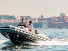 A lively group enjoys a thrilling ride on a Clubman boat, showcasing the excitement of on-water adventures against a scenic city backdrop.