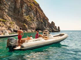 A family enjoys a sunny day on the water, interacting on a boat near a stunning coastline — perfect for memorable boating adventures.