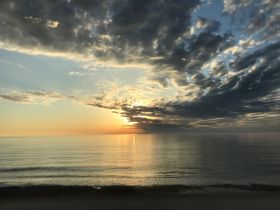 A serene sunset over calm waters, showcasing a beautiful sky filled with clouds and warm hues — perfect for tranquil moments by the sea.