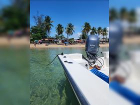 A clear view of a speedboat anchored near a sandy beach, surrounded by palm trees and vibrant umbrellas, perfect for a day of relaxation and fun on the water.