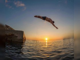 A person leaps into the water at sunset, capturing the thrill of summer adventures and water activities. Perfect for showcasing fun moments during a boat trip.