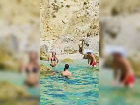 A lively group enjoys a refreshing swim in crystal-clear waters, surrounded by stunning rock formations — perfect for beach fun and relaxation.