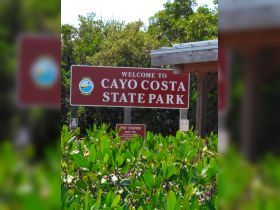 Welcome sign for Cayo Costa State Park, providing information about park fees and regulations, surrounded by lush greenery.