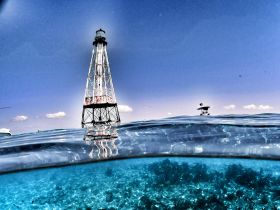 A stunning split-shot of a lighthouse above water, with vibrant underwater scenery visible — a perfect representation of coastal adventures and exploration.