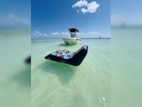 A colorful floating mat is anchored in shallow waters near a boat, perfect for relaxing and enjoying the sun on a day out at sea.