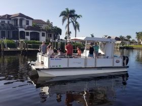 A lively group waves from the deck of the 'Miss Gabriella' pontoon boat, enjoying a sunny day on the water — perfect for family outings or group celebrations.