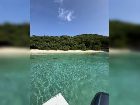 A serene view of a pristine beach surrounded by lush greenery and clear turquoise waters, perfect for a relaxing day on the water.