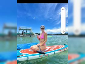 A woman enjoys paddleboarding in clear waters, showcasing a fun day of water activities under a bright blue sky.
