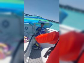 A young boy relaxes under a colorful umbrella on a boat, showcasing a cozy interior space perfect for shade and comfort during a sunny day on the water.
