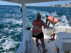 Two individuals actively engage in fishing aboard a boat, showcasing the excitement of on-water activities and group fun.