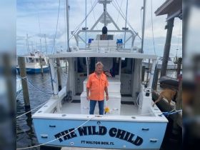 A man stands proudly on the deck of the 'Wild Child' boat at the dock, showcasing the vessel's name and inviting atmosphere for fishing adventures in Fort Walton Beach, FL.