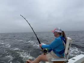 A woman enjoys a fishing experience on a boat, showcasing the thrill of on-water activities in a cloudy setting.