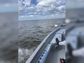 A view from the side of a boat cruising on open water, showcasing the vessel's design and the expansive sky above.