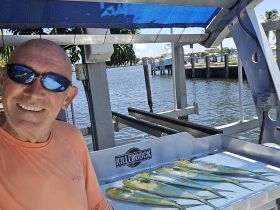 A smiling angler poses with a fresh catch of fish on a boat, showcasing a successful day of fishing in a scenic waterfront setting.