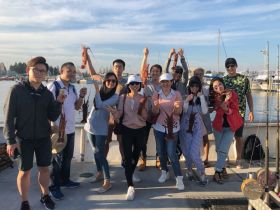 A lively group celebrates their successful lobster catch aboard a fishing boat, showcasing their haul against a picturesque marina backdrop.