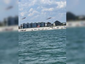 A vibrant beach scene featuring people enjoying the sun and flying kites, with colorful kites soaring above the shoreline — a perfect summer day at the beach.