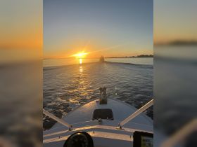 A stunning sunset view from the bow of a boat, showcasing the tranquil waters and another vessel in the distance, perfect for evening cruises.