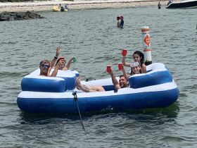 A lively group enjoys a fun day on a floating mat, celebrating with drinks and good vibes in the water — perfect for summer outings and parties.