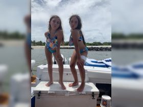 Two girls pose playfully on a boat, showcasing their colorful swimsuits and enjoying a fun day on the water — perfect for family outings or beach adventures.