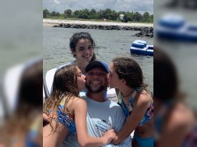 A joyful family moment on a boat as two girls kiss their father, capturing a heartwarming celebration of love and togetherness on the water.