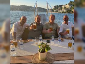 A group of friends raises their glasses in a toast aboard a boat, enjoying drinks and camaraderie against a scenic waterfront backdrop.