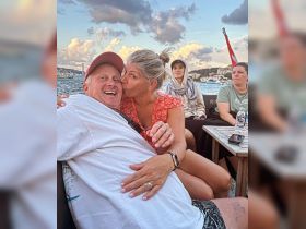 A joyful couple shares a kiss aboard a boat, surrounded by friends and stunning scenery — perfect for memorable moments on the water.