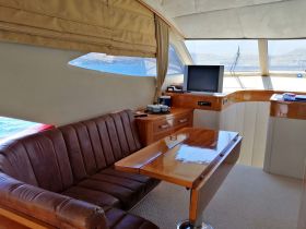 Inside view of a luxurious boat cabin featuring comfortable seating and a polished wooden table, perfect for relaxing or dining while enjoying the sea views.