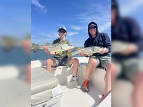 A father and son proudly display their catch of snook while enjoying a day of fishing on the water — a perfect bonding experience for families.
