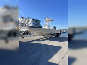 A sleek boat on its trailer at the dock, showcasing its design against a clear blue sky and a cruise ship in the background.