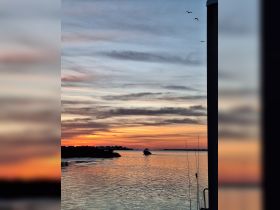 A stunning sunset over the water with a boat cruising along the coastline, creating a picturesque scene perfect for evening adventures.